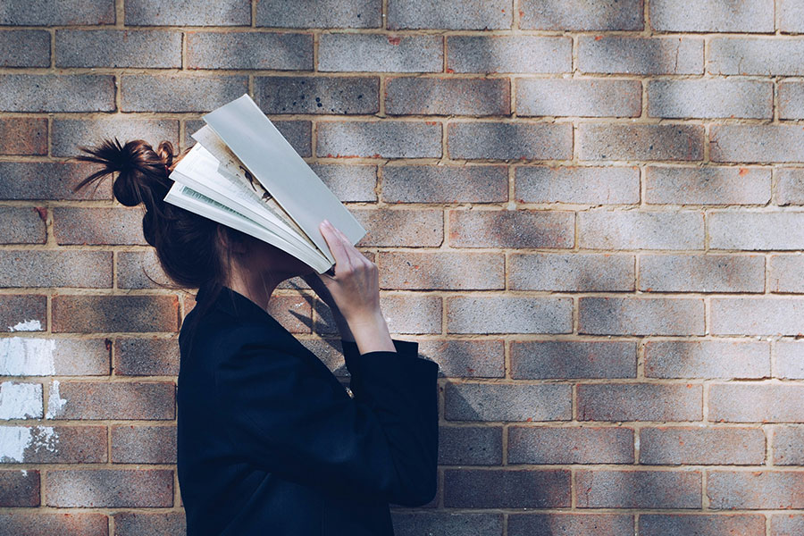 a girl with a messy bun slams a book to her face while walking